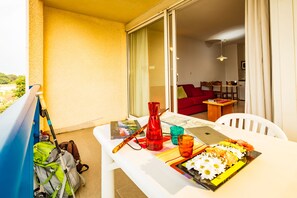 Un balcón con una mesa lista para comer, un florero rojo y una computadora portátil.