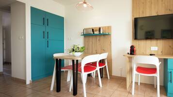 Una cocina moderna con armarios color turquesa, encimera de madera, una mesa de comedor con sillas blancas y un televisor montado en la pared.