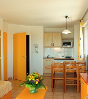 Cocina compacta con microondas, estufa y comedor con sillas y mesa de madera.