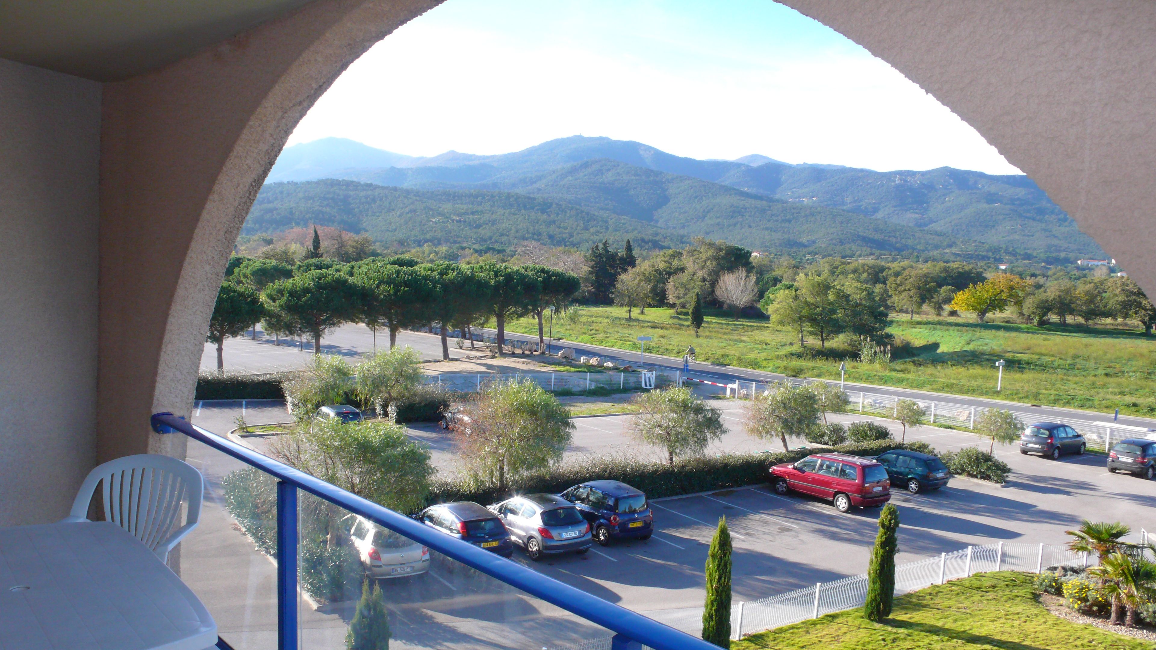 Un balcón con vista a un estacionamiento y montañas a lo lejos.