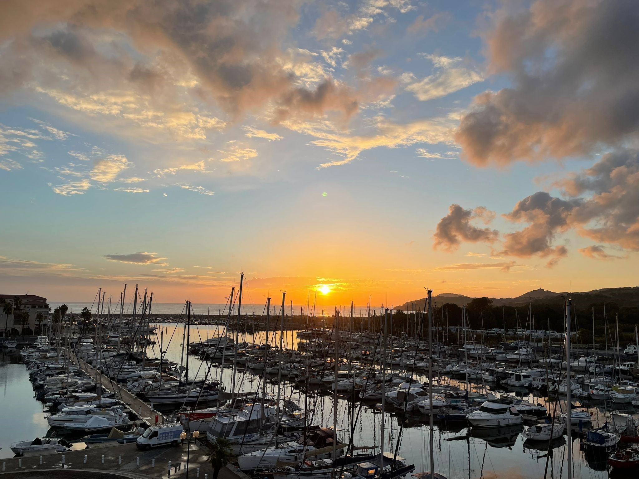 Un puerto deportivo con numerosos barcos amarrados, una masa de agua tranquila y una puesta de sol al fondo.