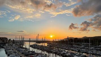 Un puerto deportivo con numerosos barcos amarrados, una masa de agua tranquila y una puesta de sol al fondo.