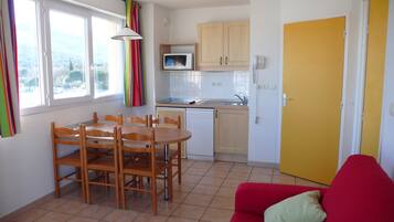 Cocina compacta con una mesa de comedor y sillas, un microondas, un lavavajillas y una puerta amarilla.
