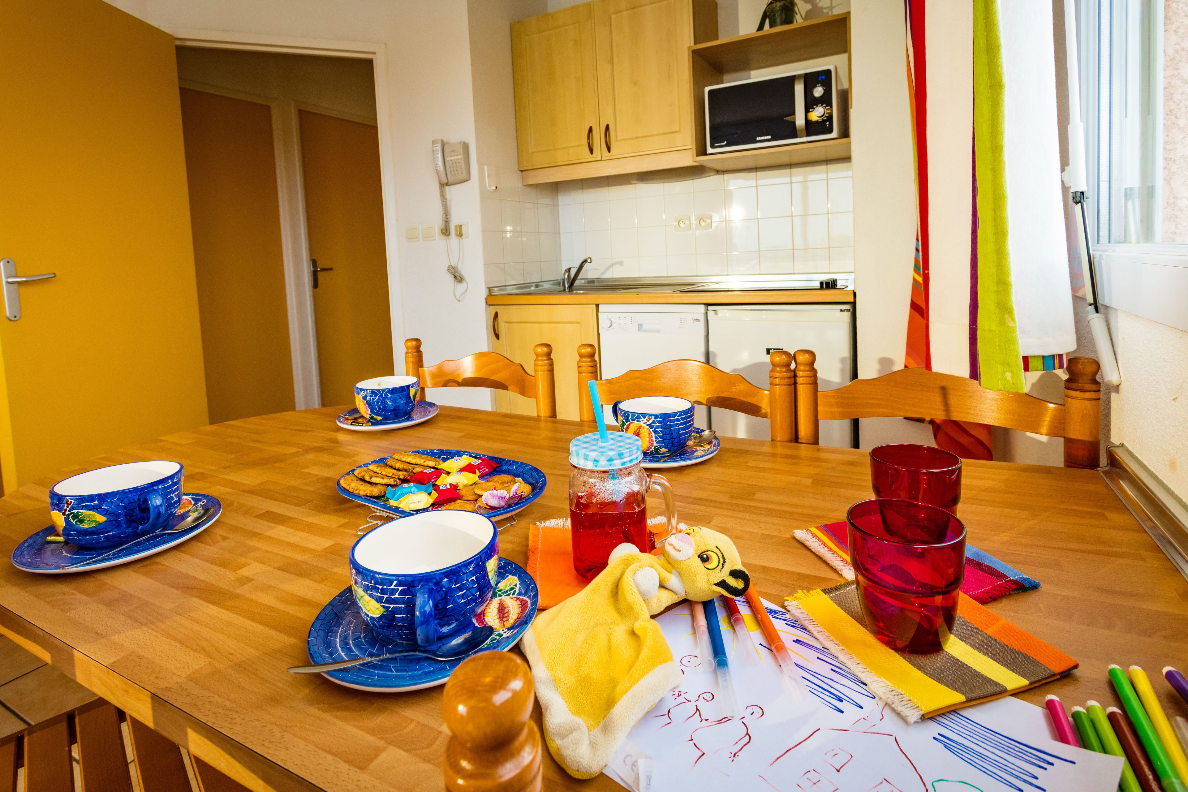 Una mesa de comedor con vajilla azul y roja, un edredón amarillo y materiales de arte.