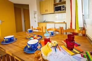 A dining table with blue and red dishes, a yellow blanket, and art supplies. - Résidence Appart-hôtel Argelès-sur-mer (Argelès-sur-Mer)
