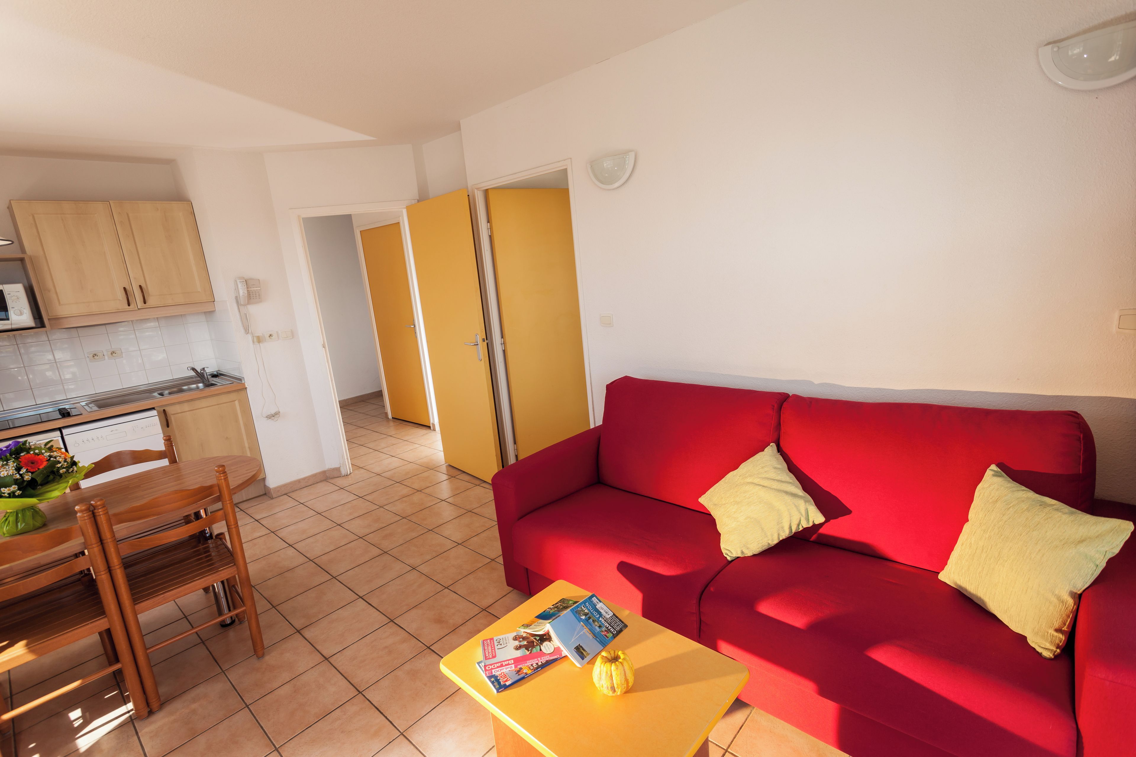Un espacio habitable compacto con un sofá rojo, una mesa de comedor de madera y una zona de cocina con armarios y un microondas.