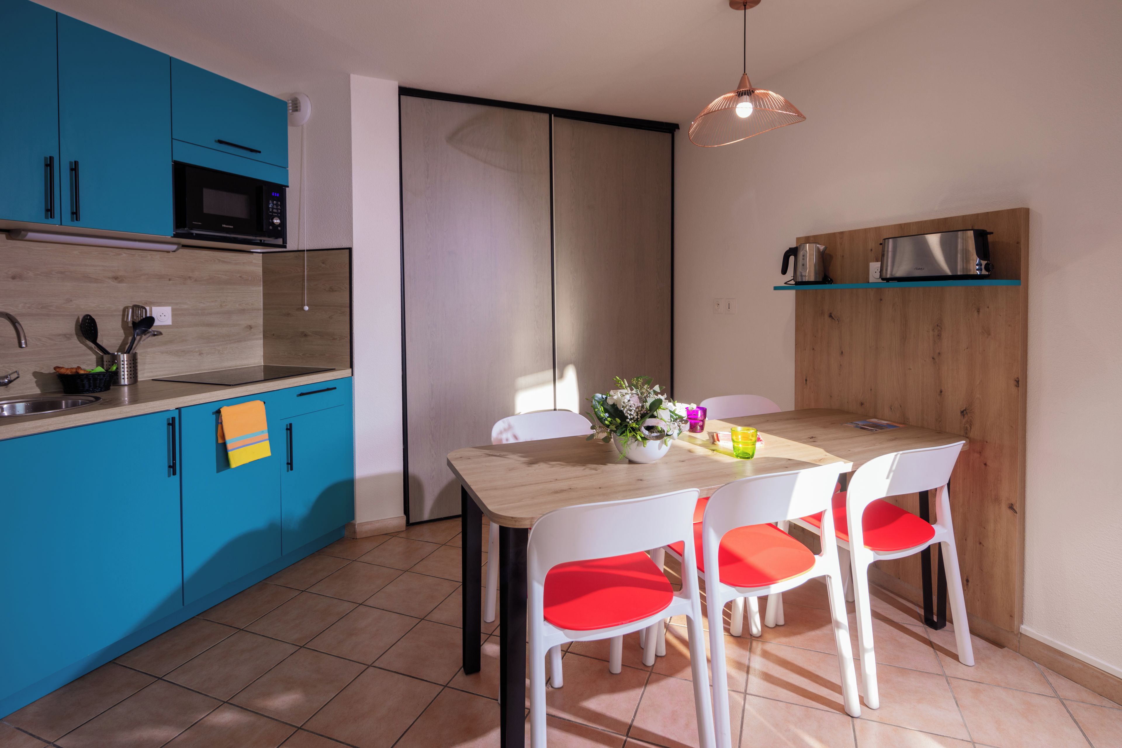 Une cuisine moderne avec des meubles bleus, un four à micro-ondes et une table à manger en bois, accompagnée de chaises blanches.