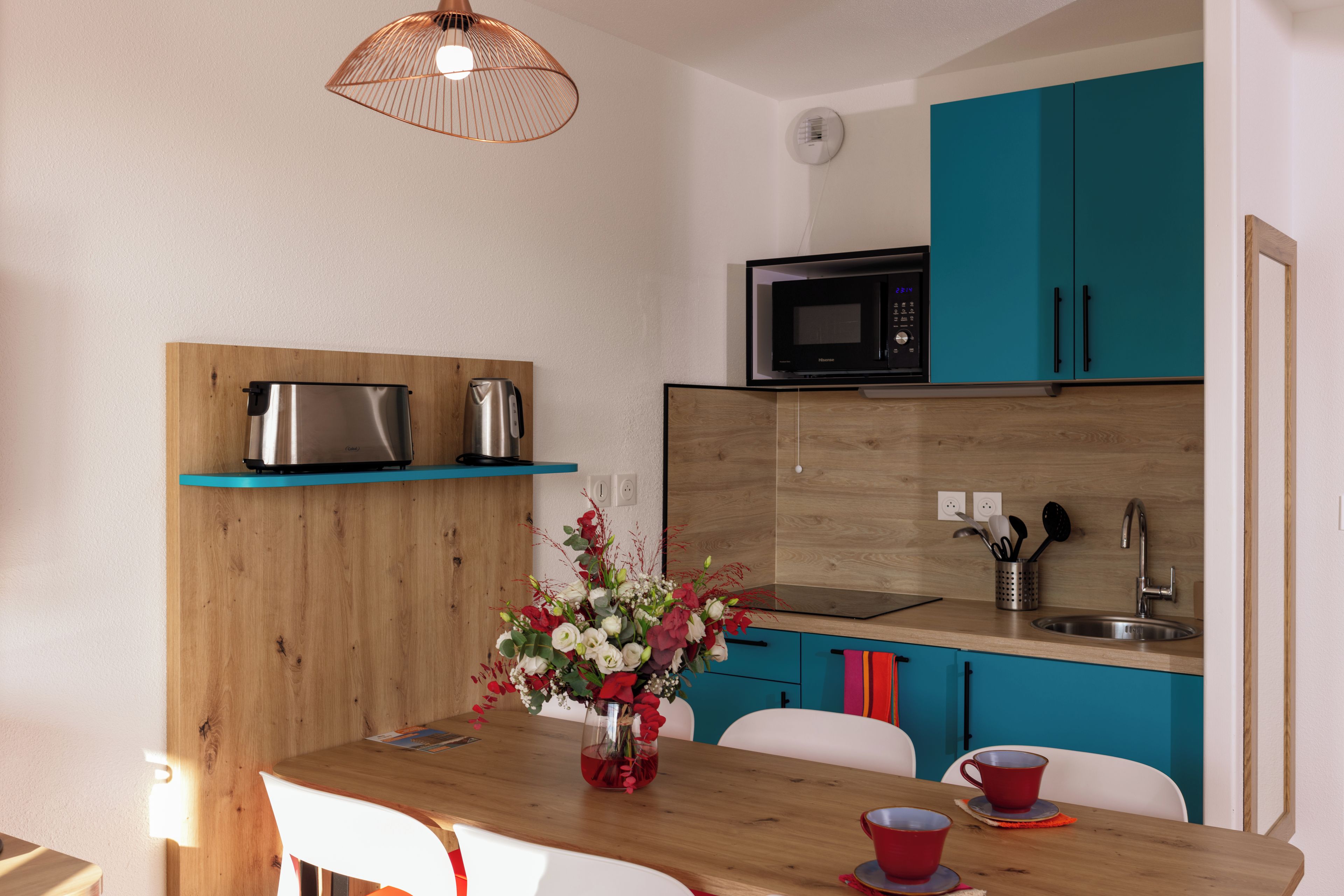 Una cocina moderna con armarios color turquesa, un microondas de acero inoxidable y una encimera de madera.