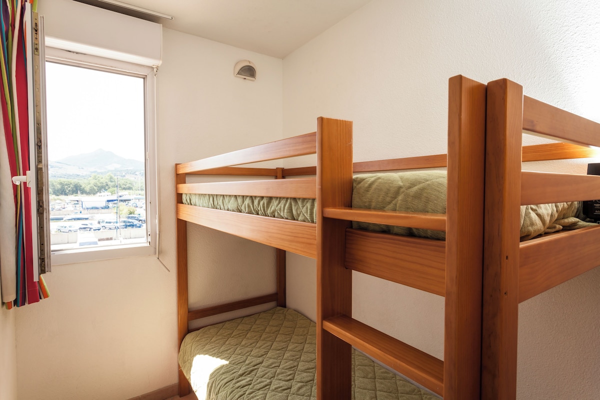 A bunk bed with a view of a parking lot and mountains through the window.