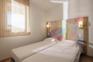A room with two single beds, a window with a curtain, a colorful abstract wall art, and two wall-mounted lamps.