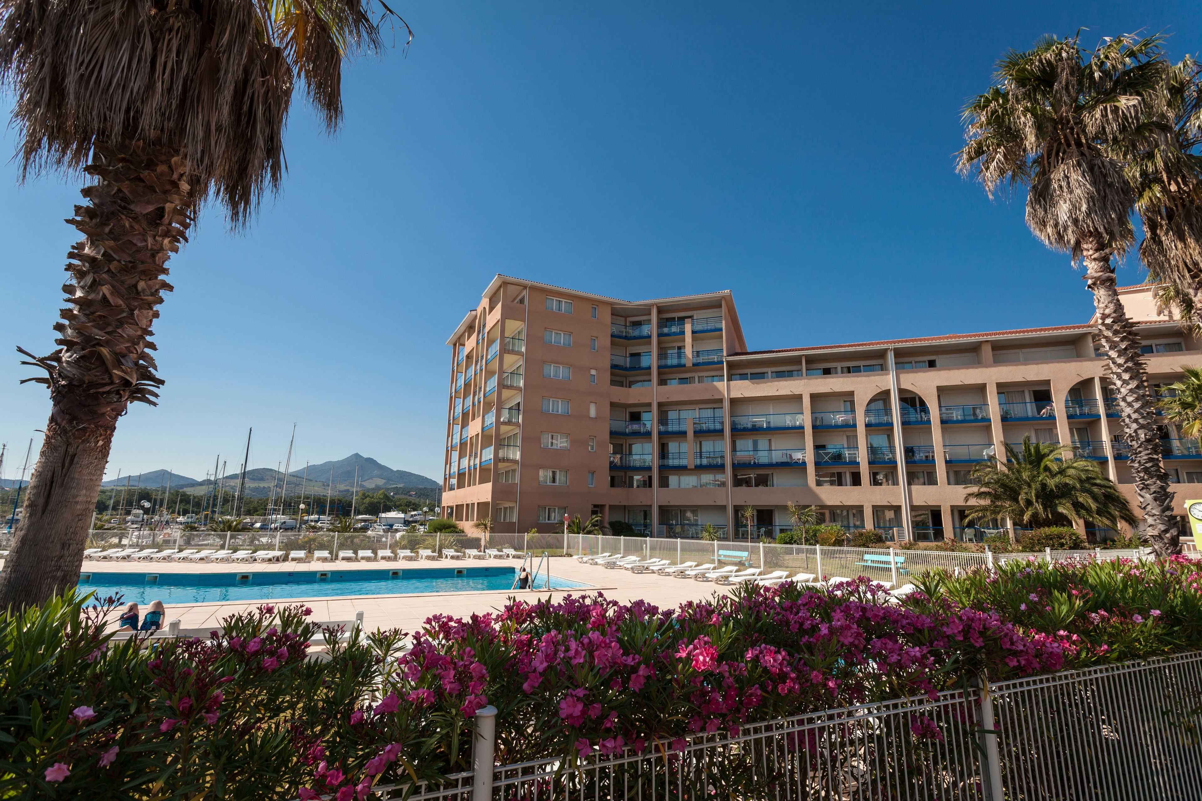 Un hotel con piscina, palmeras y un cielo azul despejado.