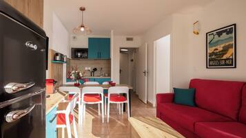 Una cocina moderna con un refrigerador negro, armarios de madera y una zona de comedor con sillas blancas y un sofá rojo.