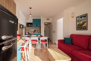 A modern kitchen with a black refrigerator, wooden cabinets, and a dining area with white chairs and a red sofa.