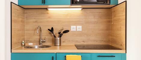 A kitchen with teal cabinets, a stainless steel sink, a microwave, and a wooden backsplash.