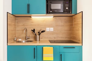 Une cuisine avec des armoires de couleur turquoise, un évier en acier inoxydable, un four à micro-ondes et un pare-feu en bois.