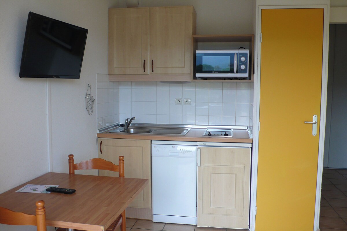 Una cocina compacta con lavavajillas, microondas y un televisor de pantalla plana montado en la pared.