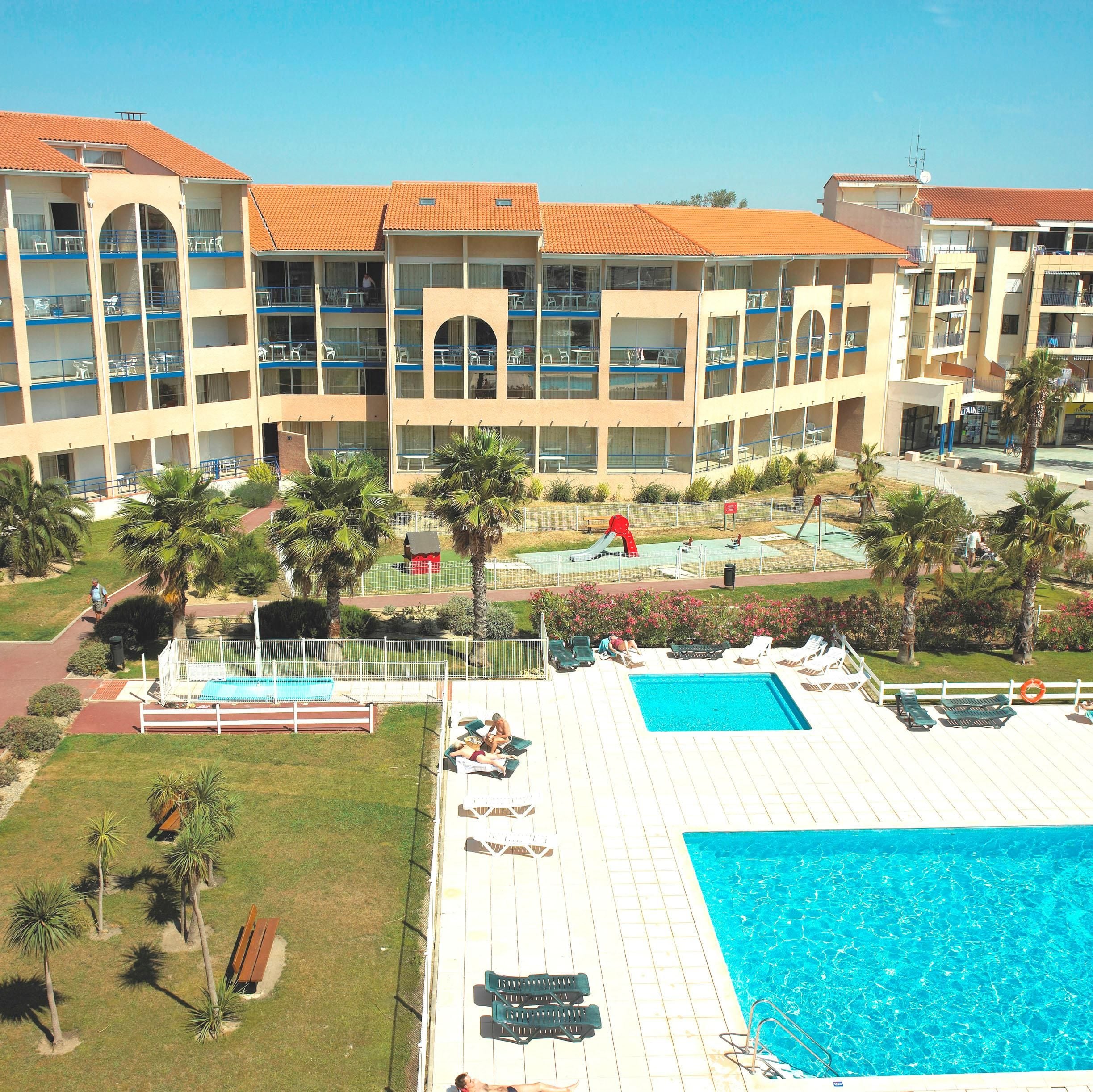 Un hotel con piscina, varios balcones y palmeras.
