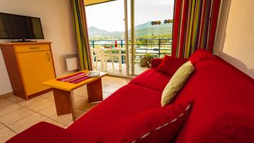 Un sofá rojo, una mesita de madera, un televisor sobre un mueble bajo y un balcón con vistas a montañas.