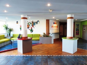 Un vestíbulo con asientos verdes, un mostrador de recepción y una pared con un mural colorido.