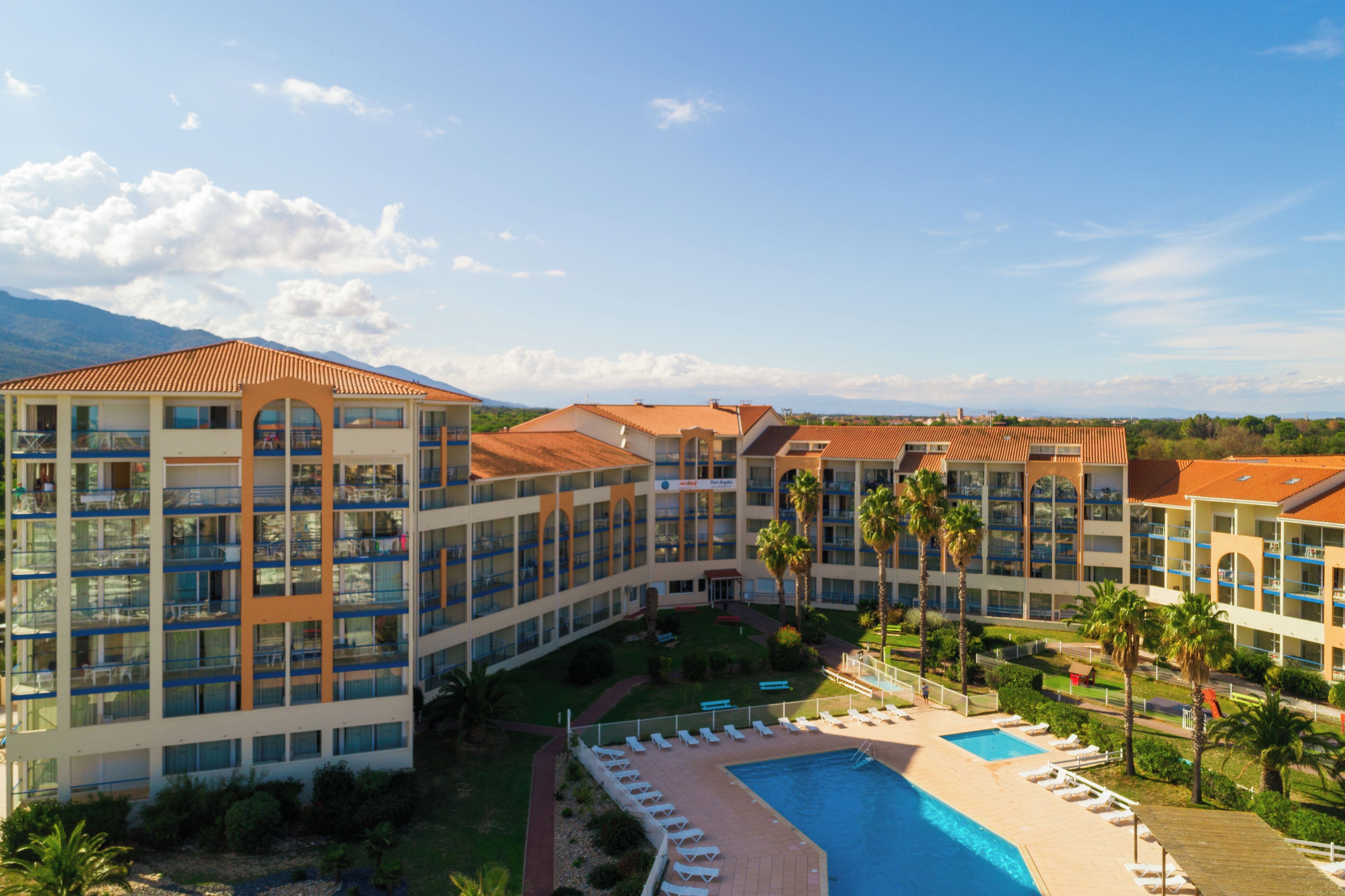 Un hotel con varias plantas, piscina y palmeras.