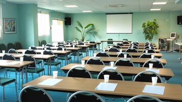 Un aula con filas de escritorios, sillas, una pantalla de proyector y una planta.