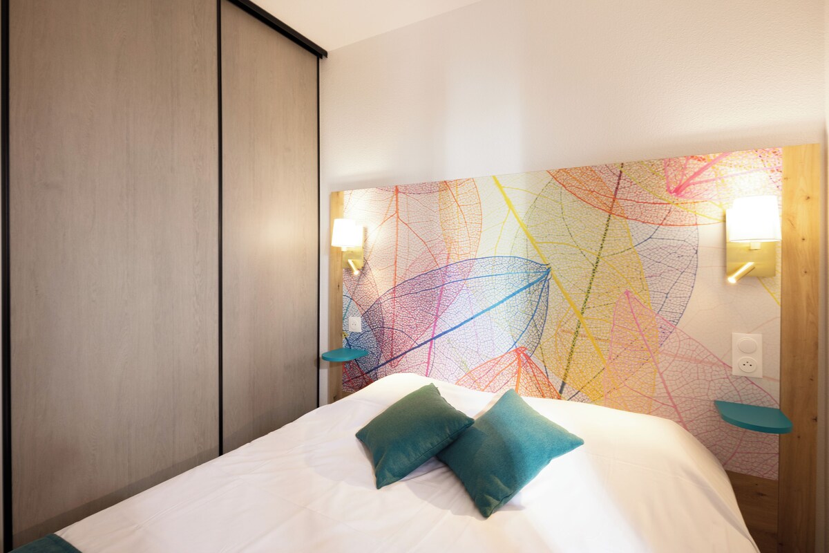 Habitación de hotel moderna con una cama grande, dos almohadas, un cuadro abstracto y colorido en la pared, y un armario de madera.