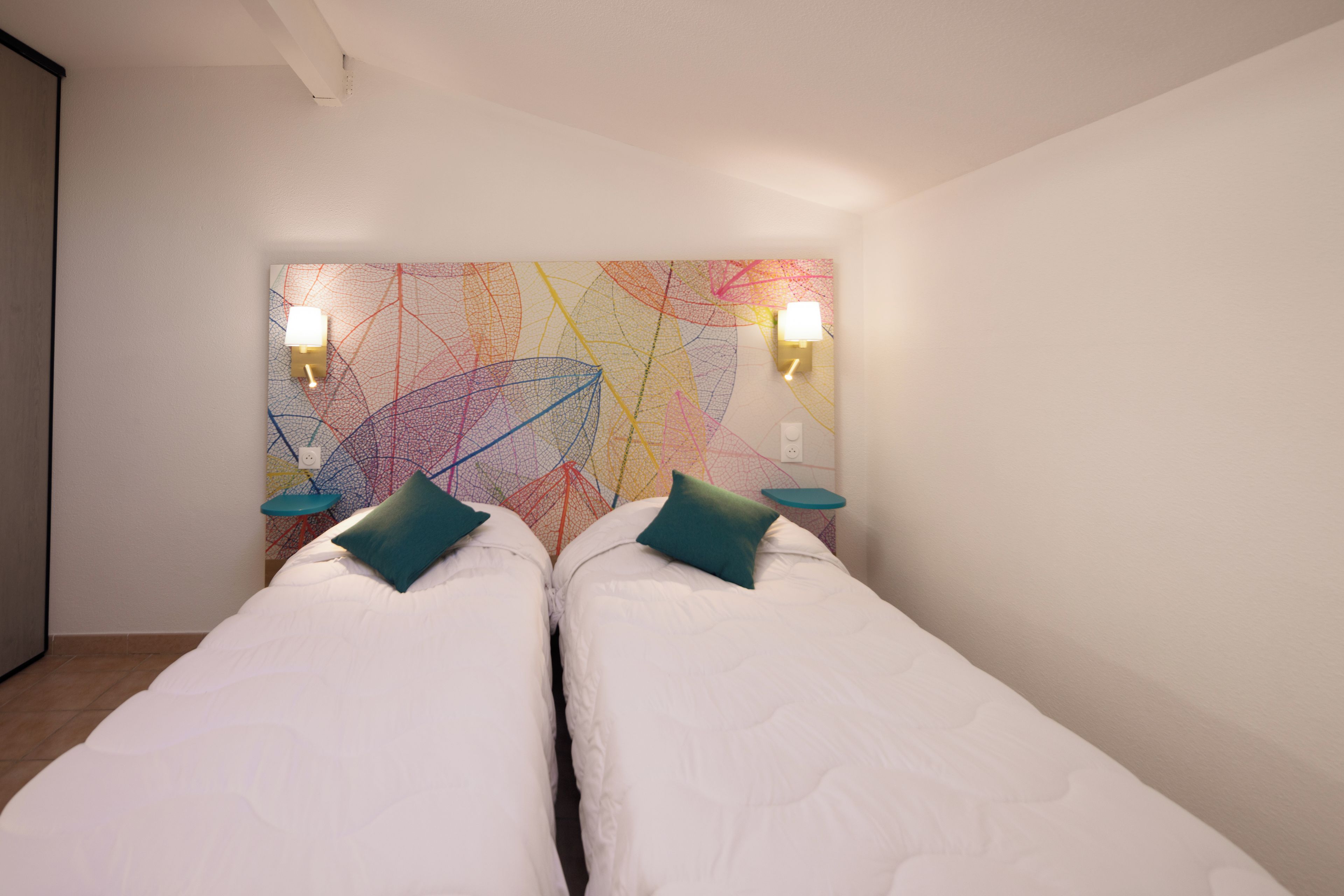 Una habitación con dos camas, un cuadro abstracto de colores y dos lámparas de pared.
