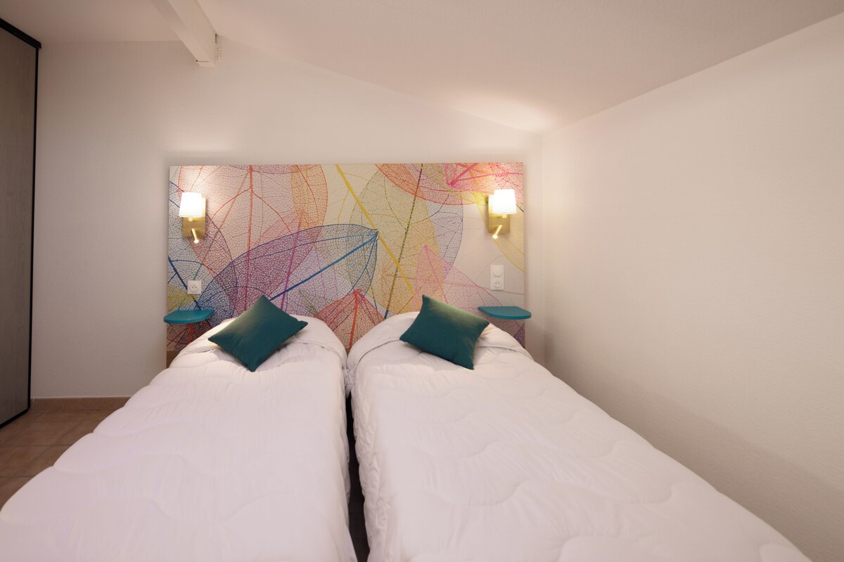 Una habitación con dos camas, un cuadro abstracto de colores y dos lámparas de pared.