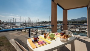 A balcony with a table set for breakfast overlooking a marina with boats and a mountain in the background.