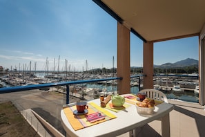 A balcony with a table set for breakfast overlooking a marina with boats and a mountain in the distance.