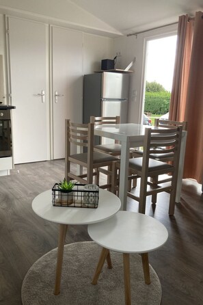 A compact kitchen with a refrigerator, a dining table with chairs, and a small round table with a plant. - Camping Hofstede Zonnevliet - Zeeuwse Knoop by Interhome (Zonnemaire)