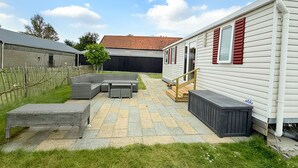 Una caravana con un patio, una terraza de madera y un jardín cercado.
