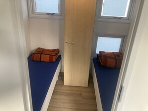 Kapea huone, jossa on kaksi sänkyä. Kummassakin sängyssä on sininen patja ja ruskea peitto. Huoneessa on kaksi ikkunaa, yksi kummallakin sivulla, ja keskellä on puinen ovi.