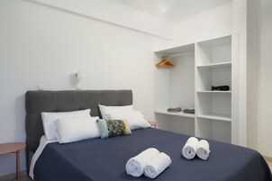 A neatly made bed with white and blue bedding, a grey headboard, and two rolled towels on the bed.