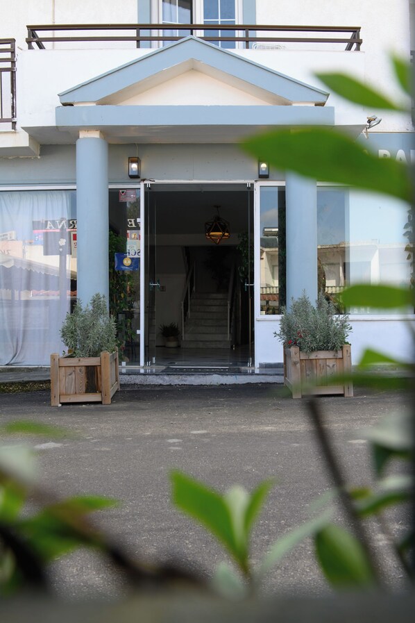 Entrada de un edificio con escaleras, plantas en macetas y vista despejada al interior.