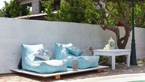 A poolside seating area with a white table and a lantern, surrounded by a white wall and greenery. - Aquarius Beach Hotel (Corfu)