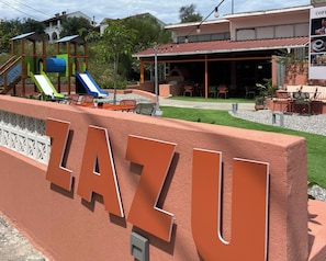A playground with slides and climbing structures, a building with outdoor seating, and a sign reading 'LAZU'. - Aquarius Beach Hotel (Corfu)