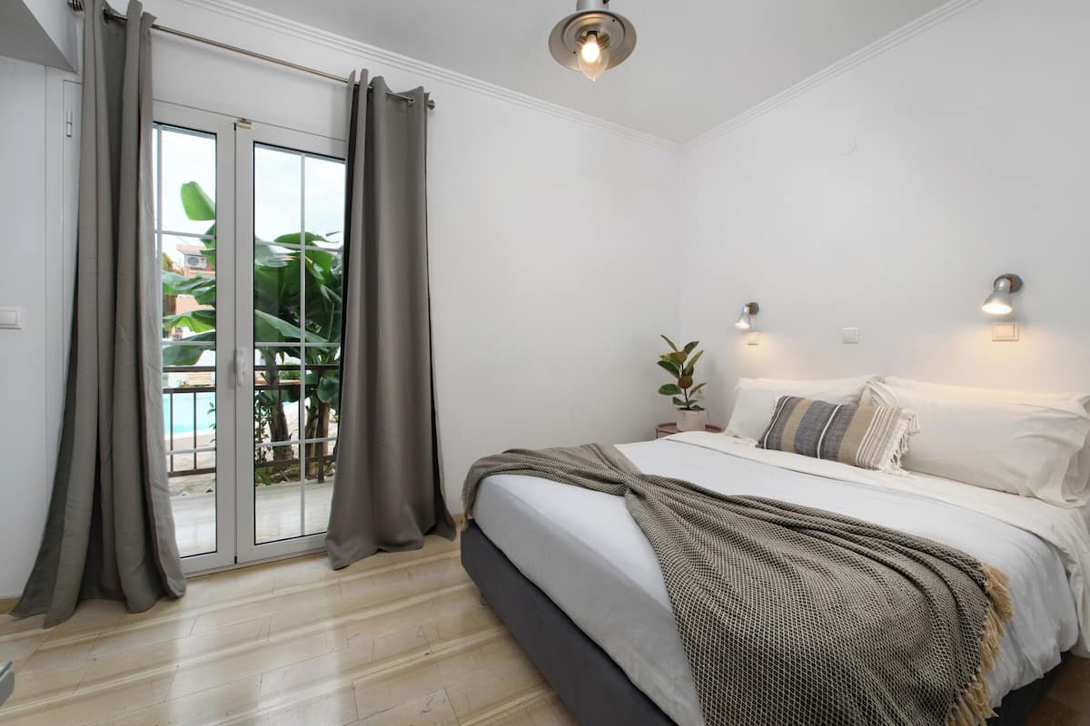 A bedroom with a bed, curtains, a ceiling light, and a view through a sliding door.