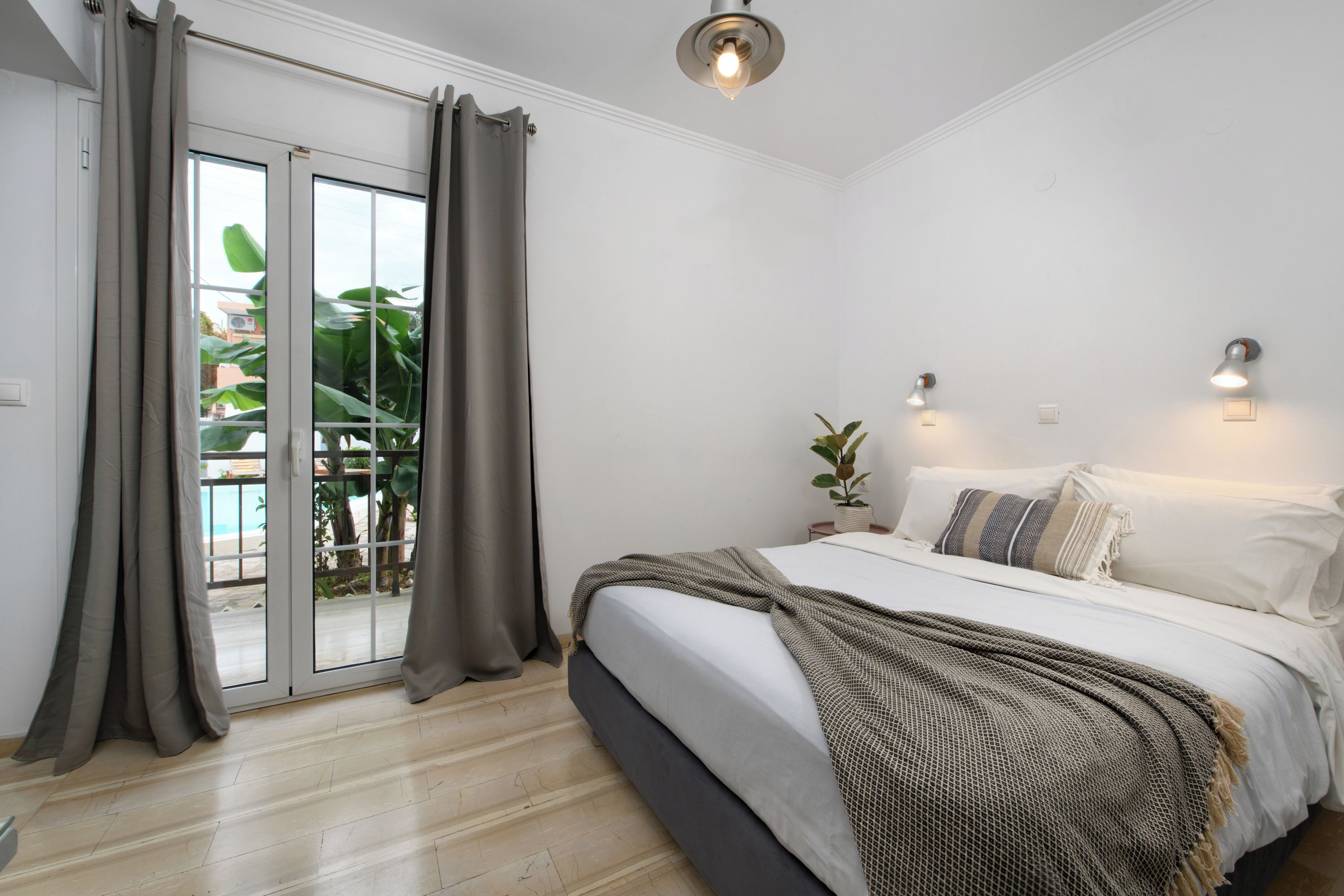 Un dormitorio con cama, cortinas, una lámpara en el techo y vistas a través de un ventanal corredero.