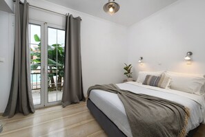 A bedroom with a bed, curtains, a ceiling light, and a view through a sliding door. - Aquarius Beach Hotel (Corfu)