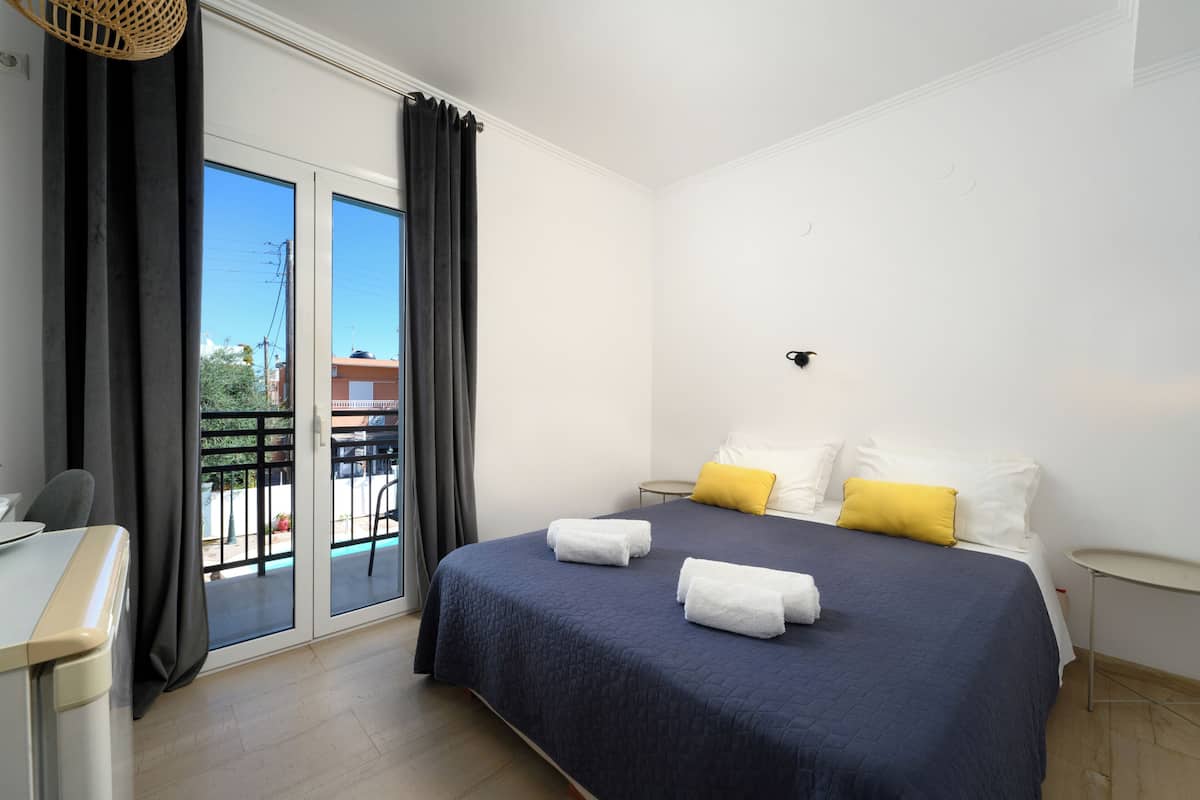 A hotel room with a bed, a desk, a chair, a small table, and a balcony with a view.