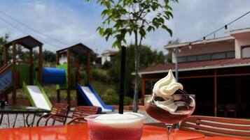 Una mesa con una bebida y un postre, un parque infantil y un edificio al fondo.