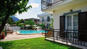 A pool area with lounge chairs, a small garden, and a building with a balcony. - Aquarius Beach Hotel (Corfu)