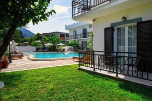 A pool area with lounge chairs, a small garden, and a building with a balcony. - Aquarius Beach Hotel (Corfu)