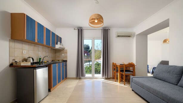 A modern kitchen with a built-in island, a dining area with a wooden table and chairs, and a grey sofa. - Aquarius Beach Hotel (Corfu)