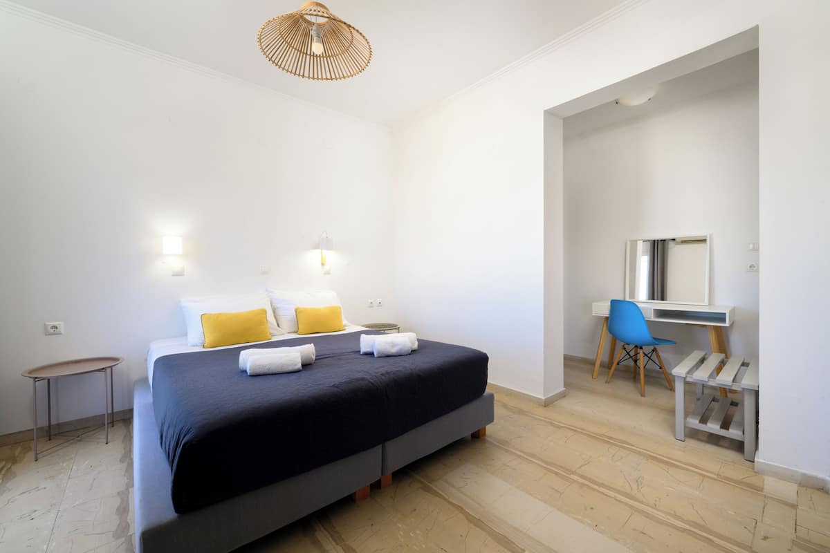 A bedroom with a bed, bedside tables, a desk, a chair, and a hanging light fixture.