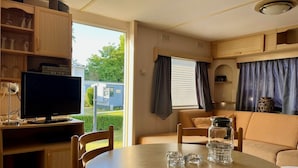 Ein kompaktes Wohnmobil-Interieur mit Esstisch, Stühlen, Fernseher und Küchenzeile.