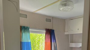 Ein Schlafzimmer mit Etagenbett, einem Fenster mit Vorhängen, einer Deckenleuchte und einem weißen Regal.