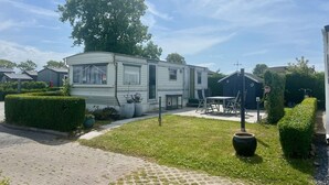 Ein Mobilheim mit einer Terrasse, einem großen Baum und einem gepflegten Rasen.