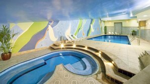 An indoor swimming pool with a unique mural, lounge chairs, and a reception area.